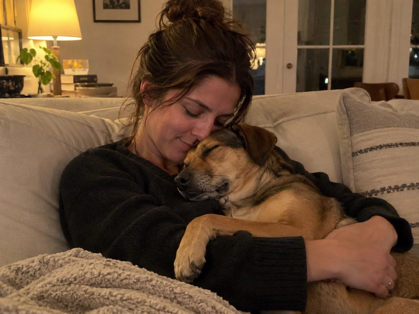 Woman holding a small nail grinder to a calm dog's paw in warm indoor light